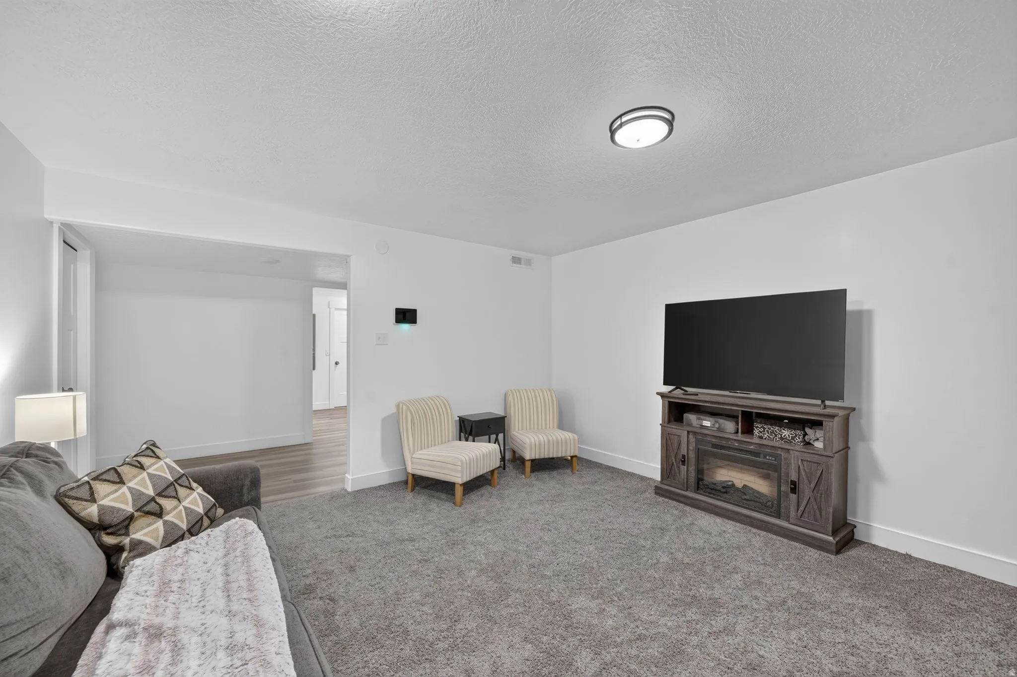 Open-concept living space featuring neutral wall tones, gray carpeting, a ceiling-mounted light fixture, and a built-in media console with an integrated electric fireplace