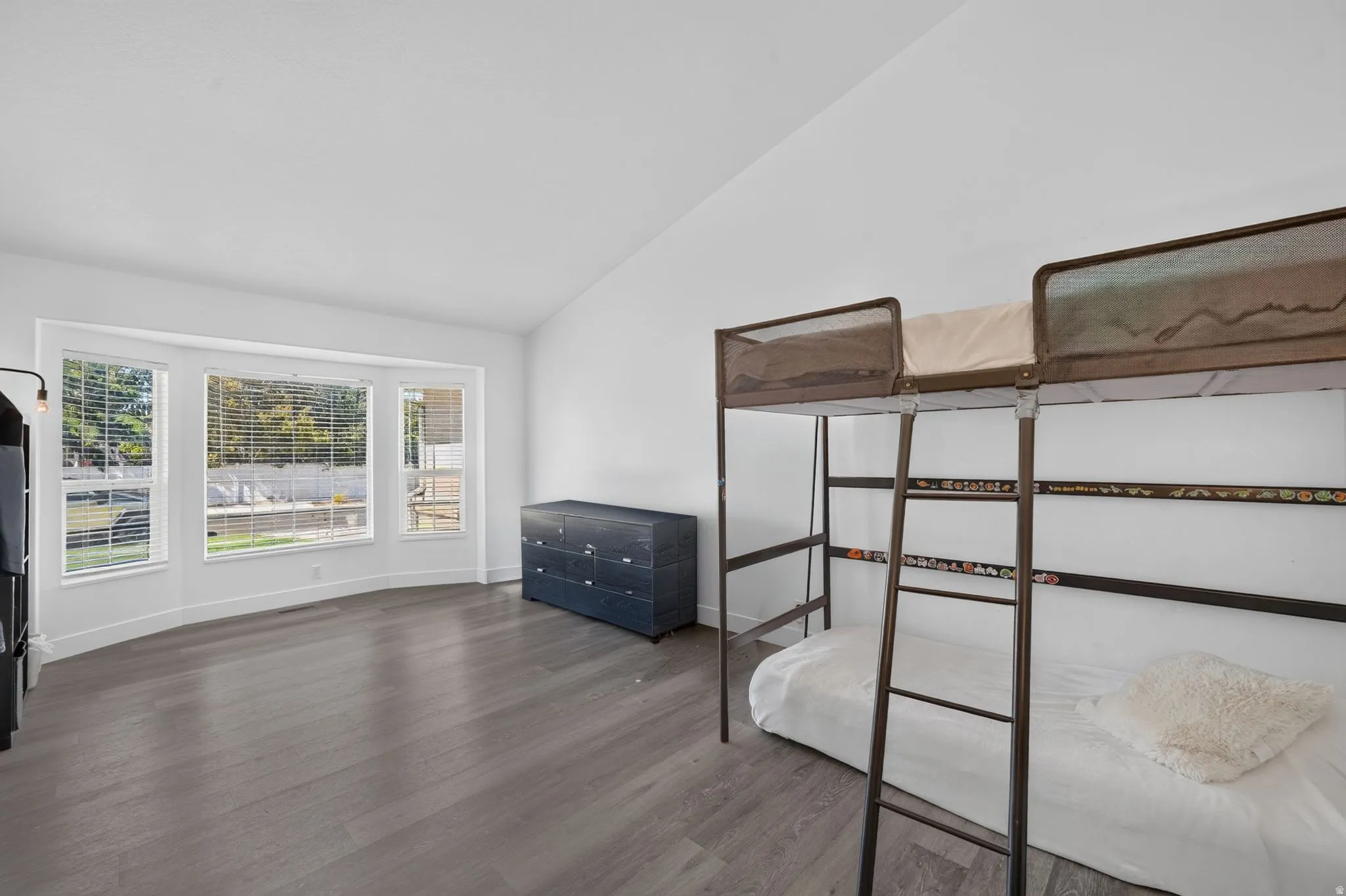 Vaulted ceilings, wood-finish flooring, white wall paint, and a bay window