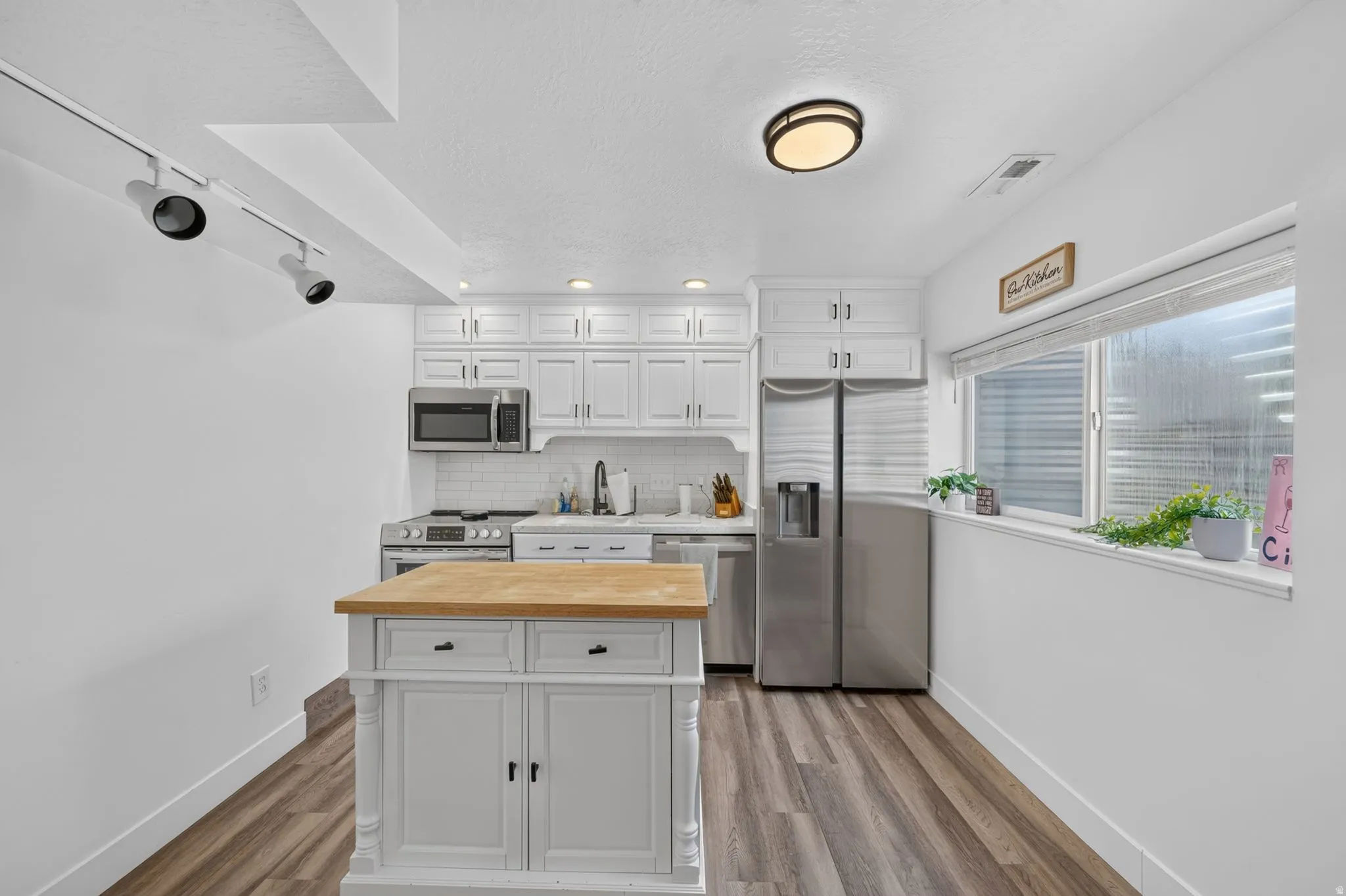 Kitchen featuring white cabinetry, stainless steel appliances, a butcher block island, wood-finish flooring, and track lighting