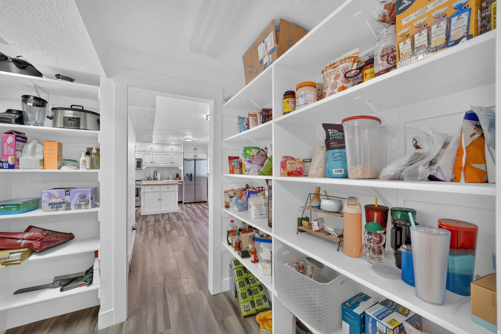 Walk-in pantry featuring built-in white shelving, wood-finish flooring, and white walls