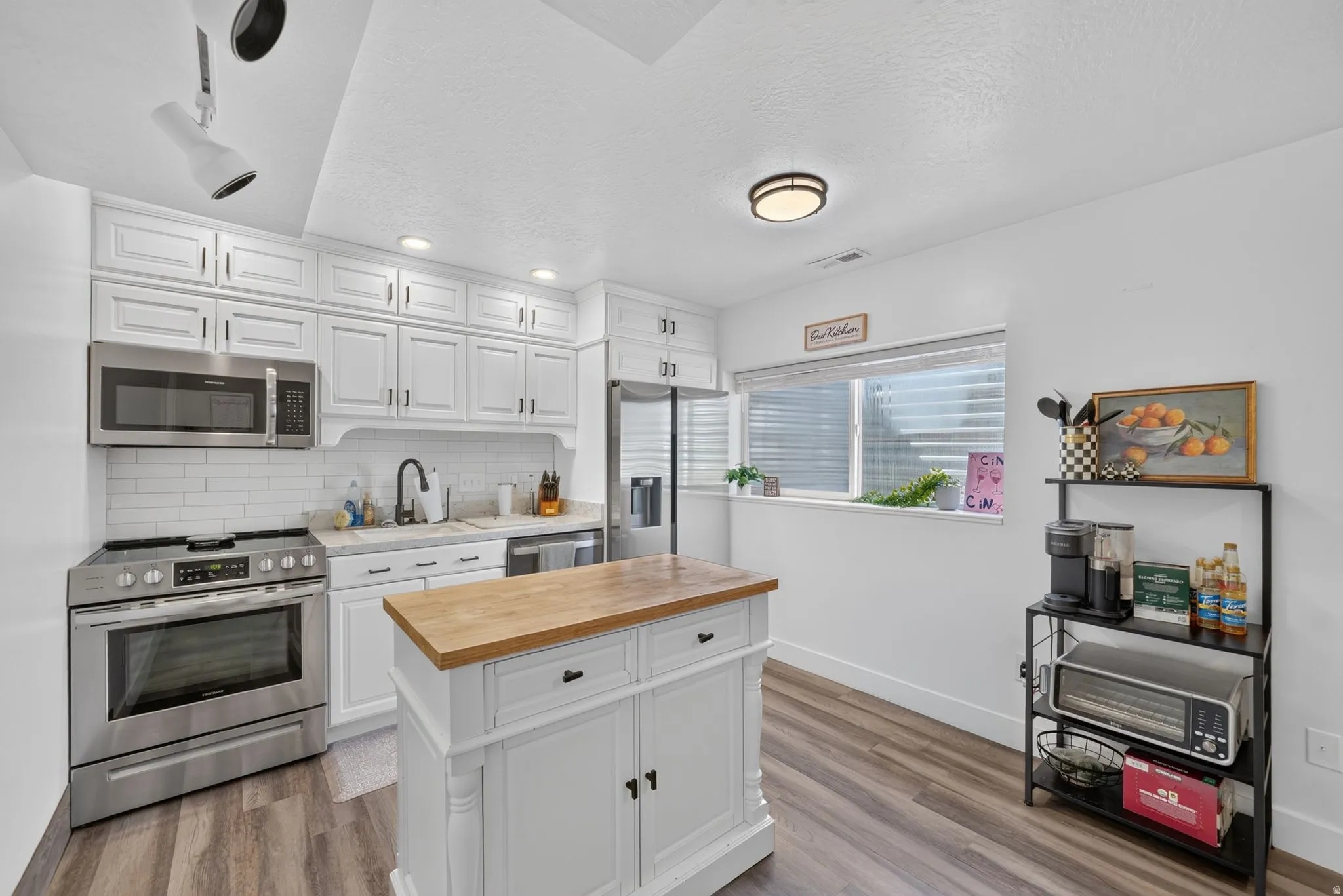 White cabinetry with modern hardware, stainless steel appliances, white subway tile backsplash, wood-finish flooring, and a central island with a wood countertop