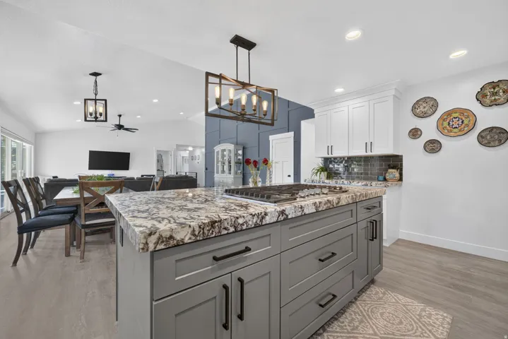 Kitchen island with built-in gas cooktop, granite-style countertop, gray shaker cabinetry, and black hardware