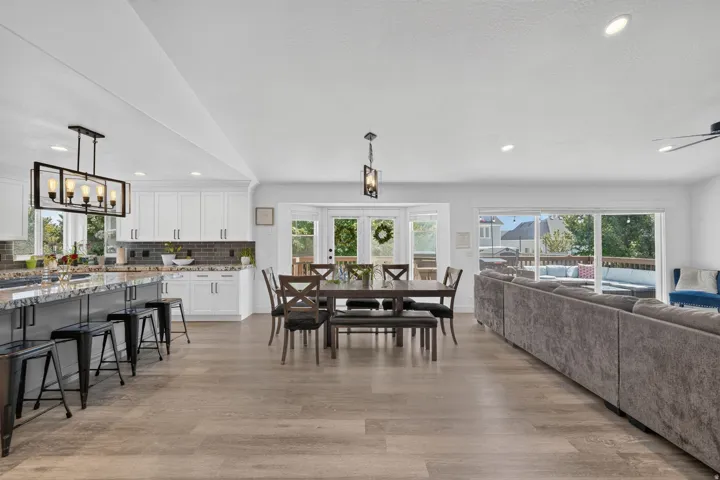 Open-concept living space featuring vaulted ceilings, wood-finish flooring, a kitchen island with stone countertop, and glass sliding doors leading to an outdoor deck