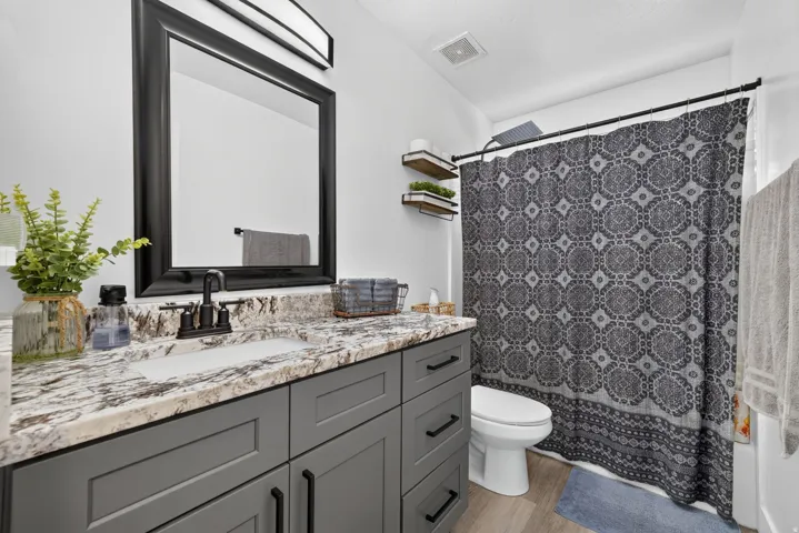 Bathroom featuring a gray vanity with black hardware, stone-finish countertop, undermount sink, and a framed mirror