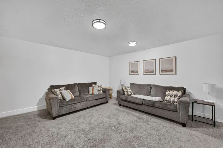Spacious recreation room featuring dual upholstered sofas, recessed ceiling lighting, neutral carpet flooring, and framed wall art