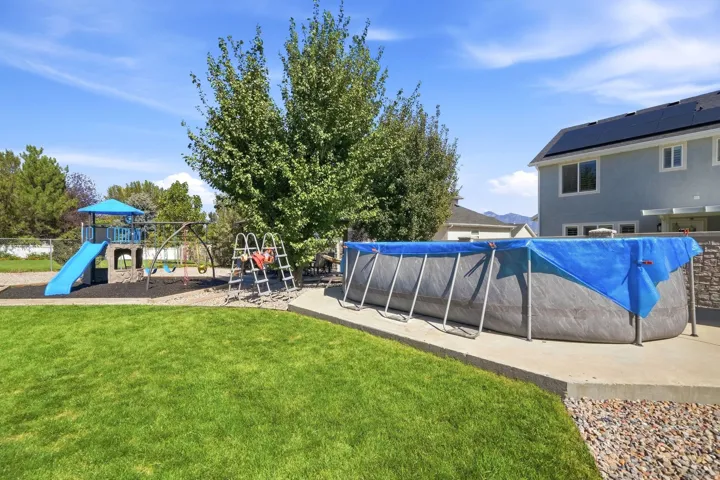 Expansive green lawn, playground structure with slide, swing set, and large above-ground pool on a concrete pad