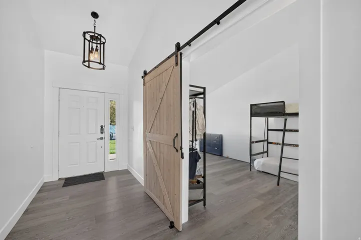 Vaulted ceiling, wood-finish flooring, white door with sidelight, black metal pendant light fixture, and a light wood-finish barn door