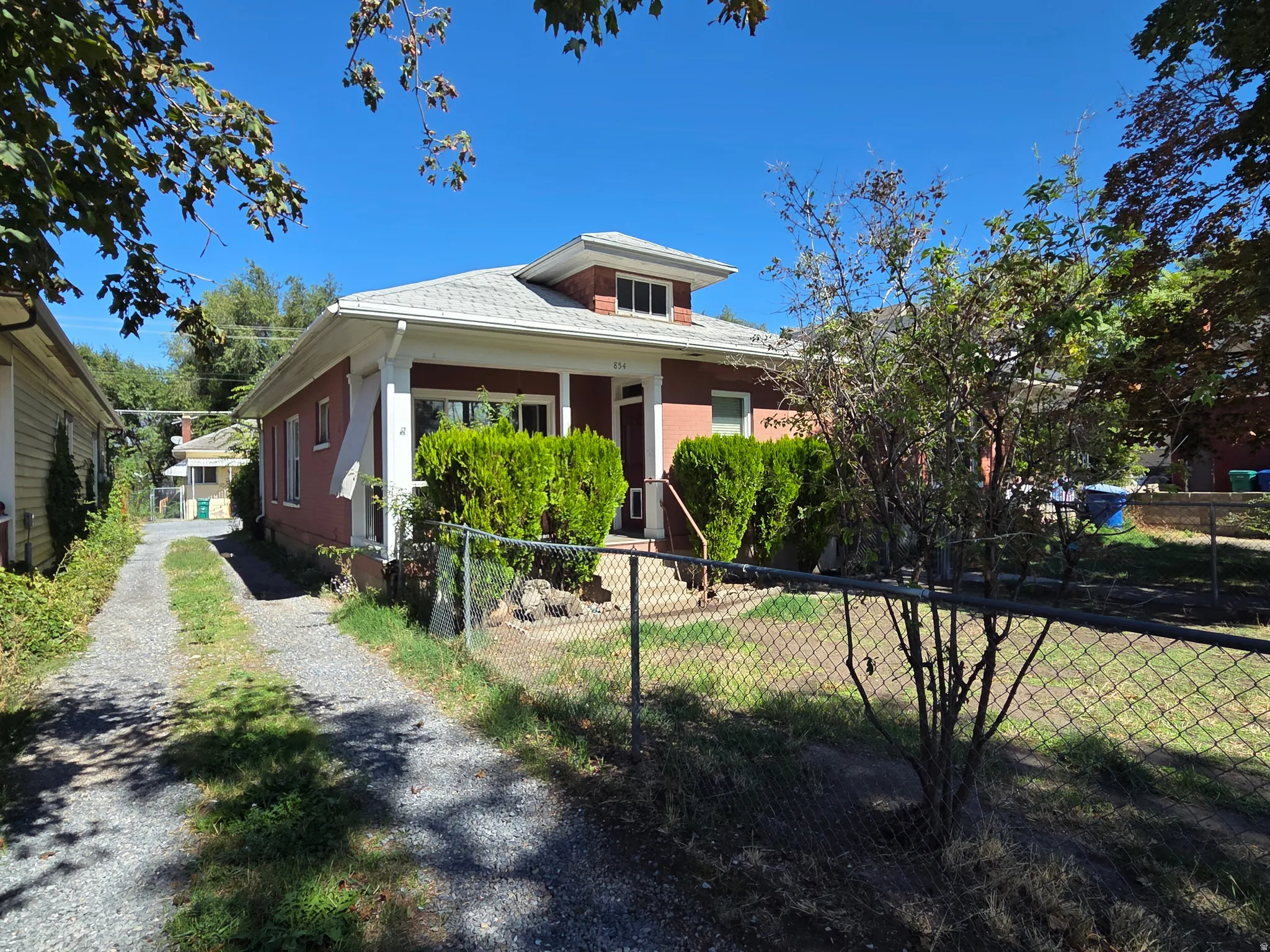 Red brick exterior with white trim, a gabled roof, and a gravel driveway