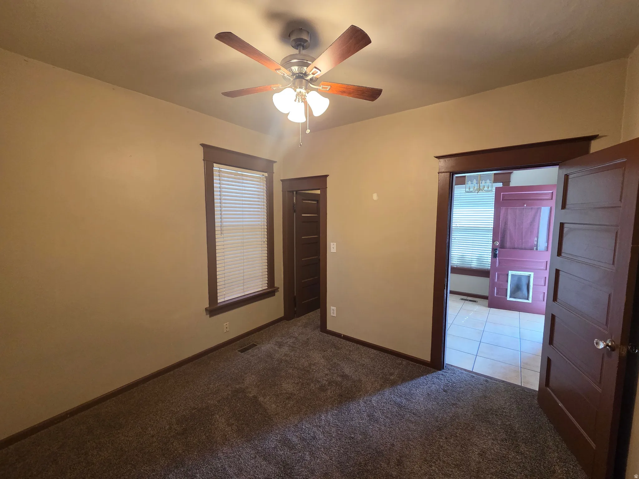 Carpeted room featuring a ceiling fan with integrated lighting, a window with horizontal blinds, and dark wood-finish trim and doors