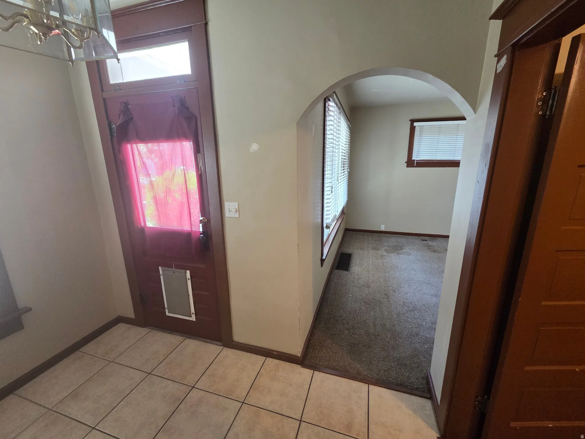 Tiled flooring entryway with a wood-paneled door, arched doorway, and interior room with windows