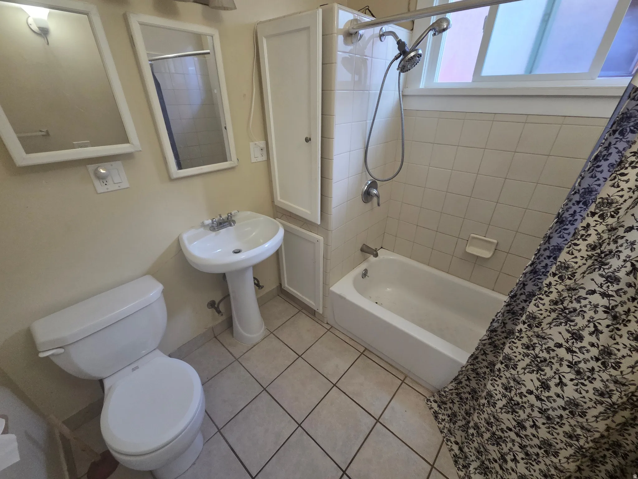 Pedestal sink with dual-handle faucet, wall-mounted mirrors, built-in storage cabinetry, and a bathtub with tiled surround