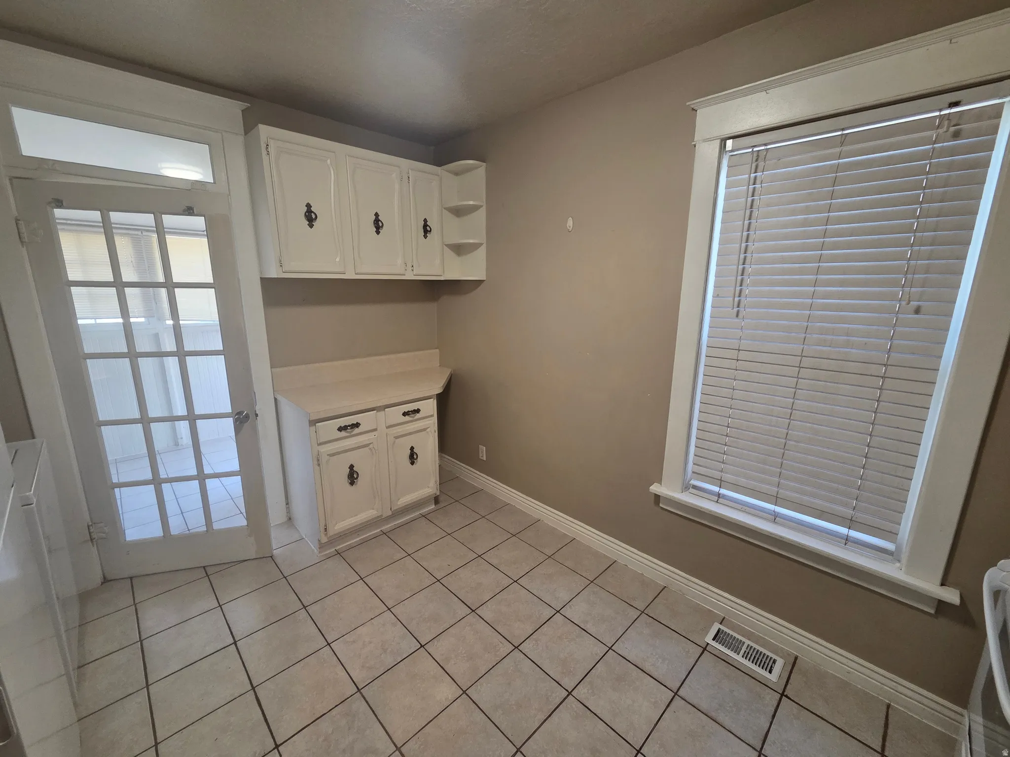 White cabinetry with built-in shelving, solid surface countertop, tile flooring, and a multi-pane glass door
