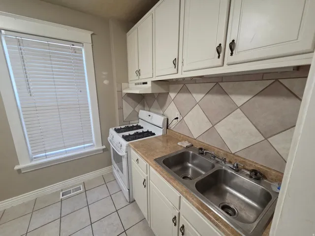 White cabinetry with dark hardware, a dual stainless steel sink, a tiled backsplash, and light-toned flooring