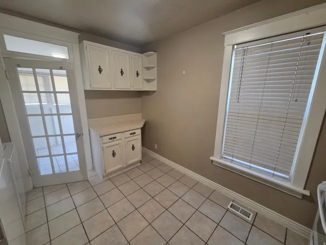 White cabinetry with built-in shelving, solid surface countertop, tile flooring, and a multi-pane glass door