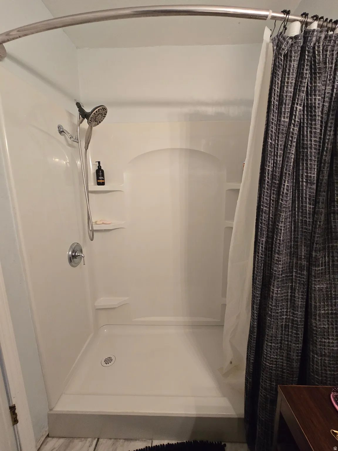 White shower stall with a handheld showerhead and built-in shelving