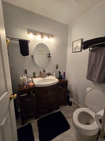 Vanity with integrated sink, wood-finish cabinetry, wall-mounted lighting, and a circular mirror