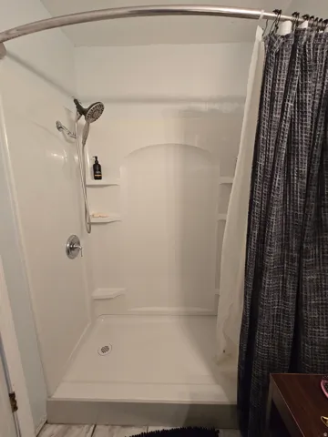 White shower stall with a handheld showerhead and built-in shelving