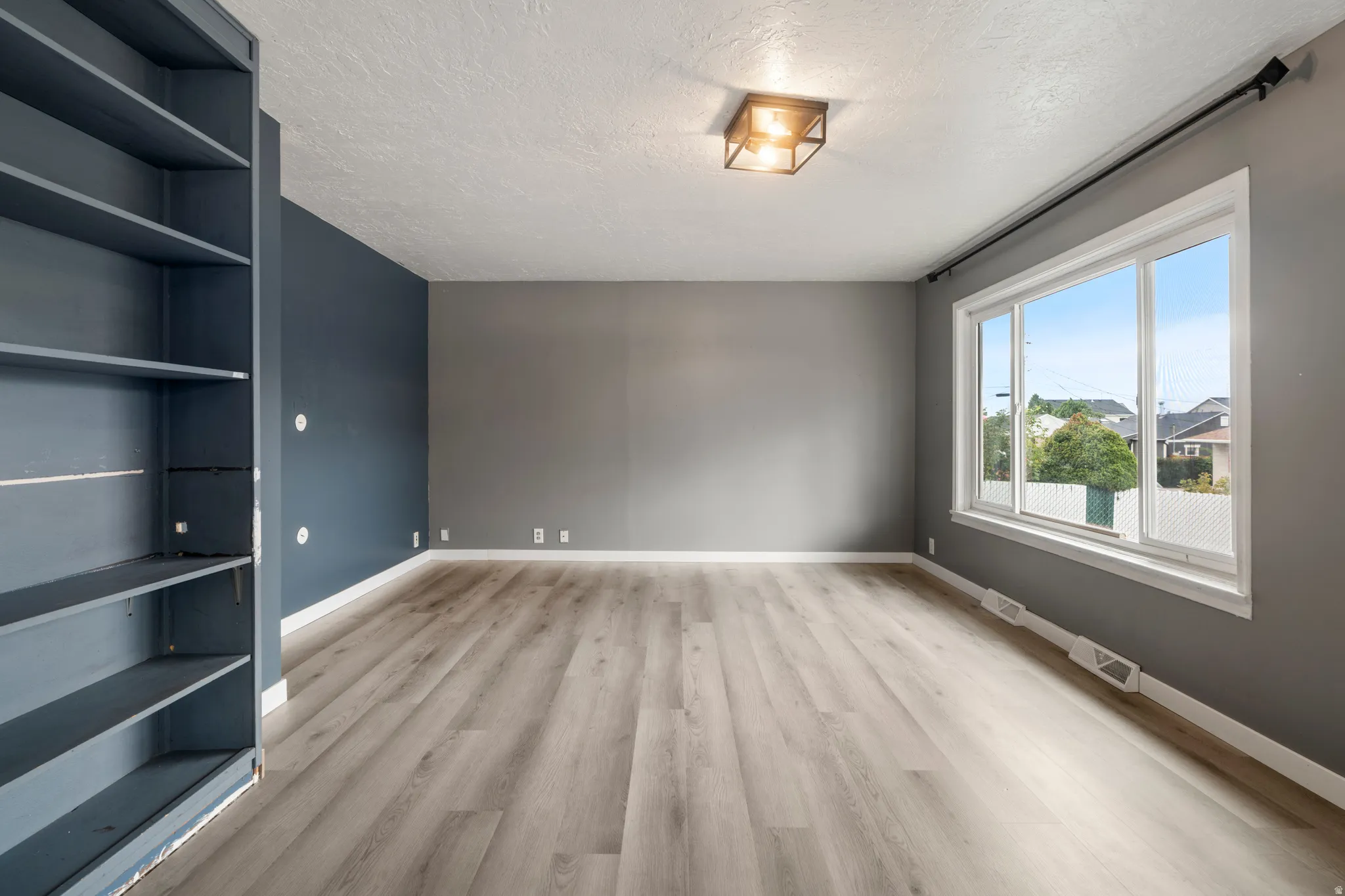 Light wood-finish flooring, built-in shelving, a large window, and a flush mount ceiling light fixture