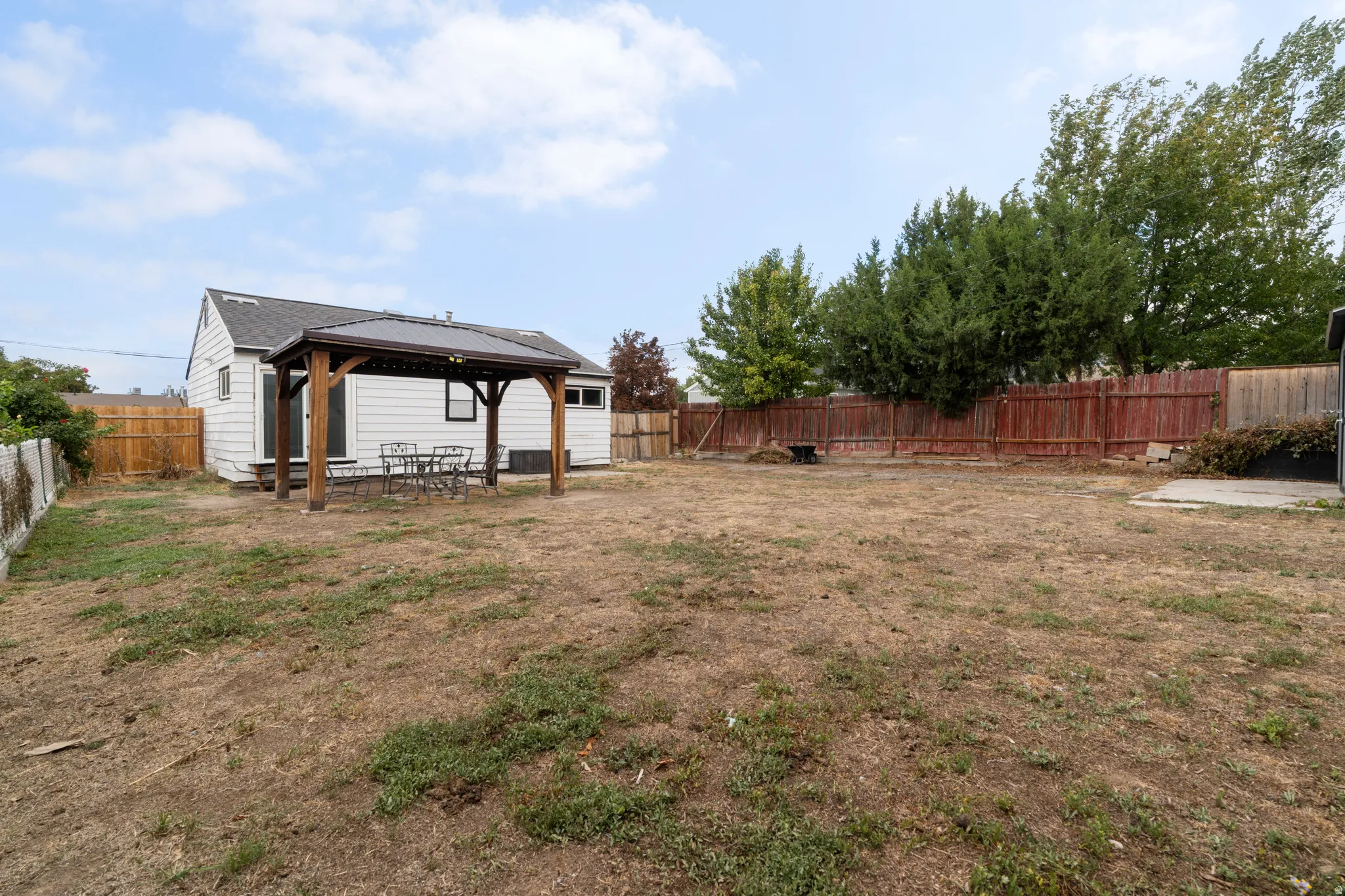 Expansive backyard featuring a wood-framed pergola with a dark roof, a white siding exterior, and a wood privacy fence