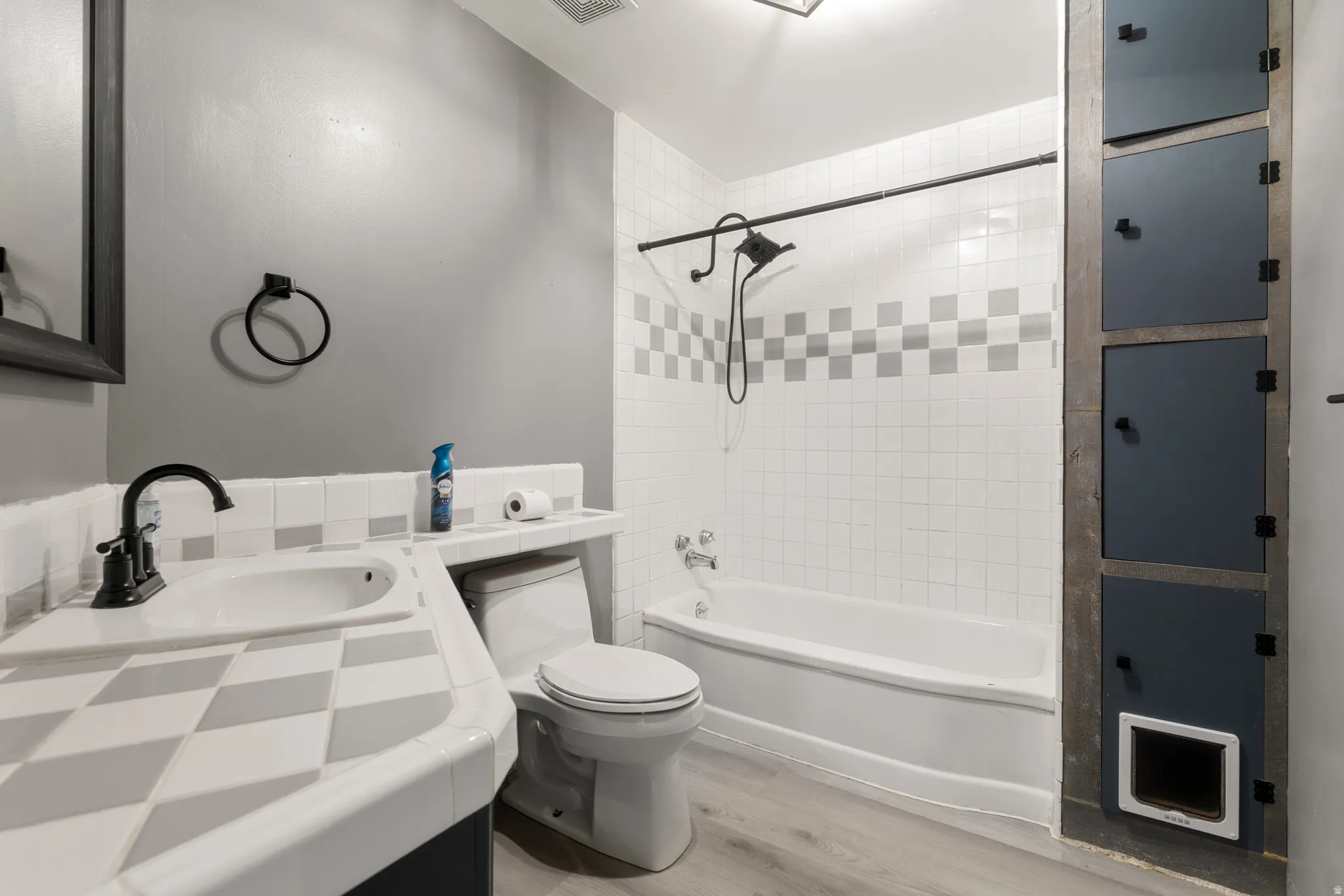 White subway tile shower surround with checkered accent band, white tub, and black shower fixtures