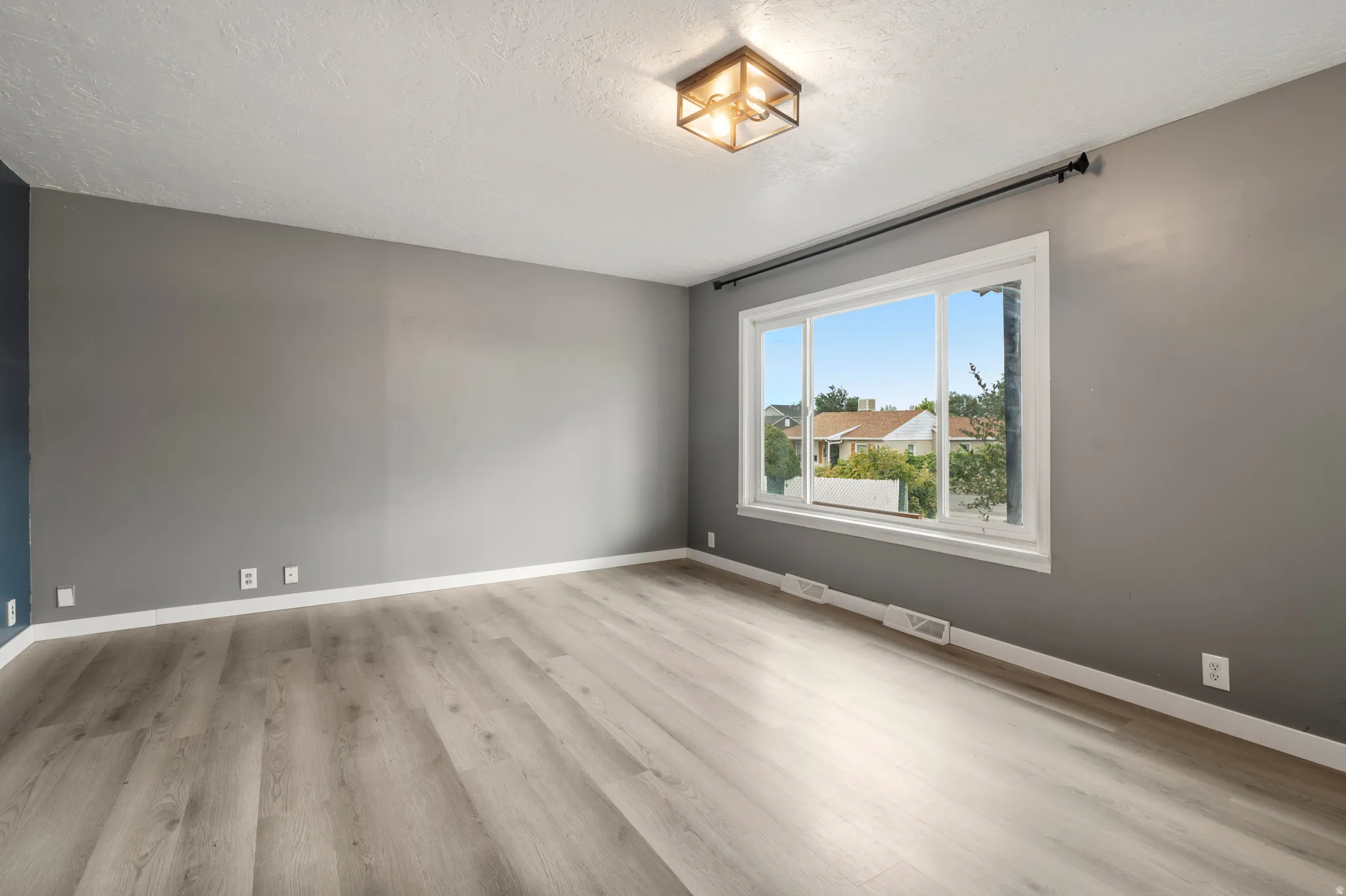 Expansive window, wood-finish flooring, contemporary ceiling light fixture, neutral wall finishes, and white trim
