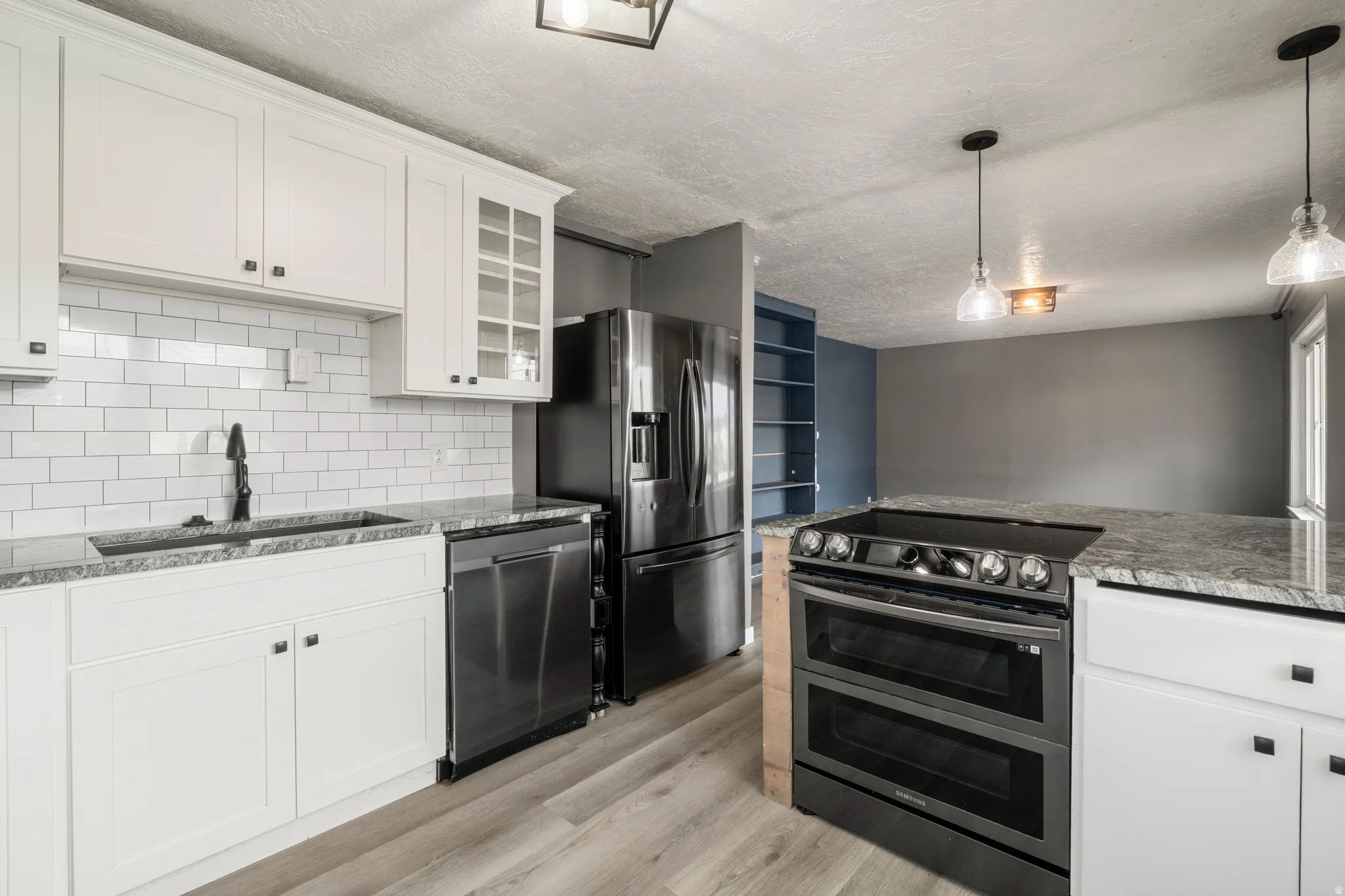 White shaker cabinetry with dark hardware, subway tile backsplash, stainless steel appliances, light-toned wood-finish flooring, and pendant lighting