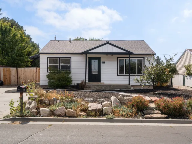 White exterior siding with black trim, covered entry, and front landscaping featuring rock elements and plantings