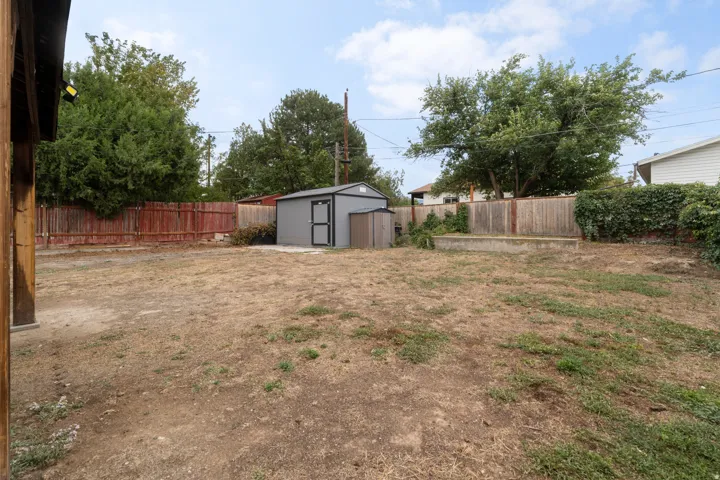 Spacious backyard featuring a metal storage shed, wood fencing, and a concrete raised planter box