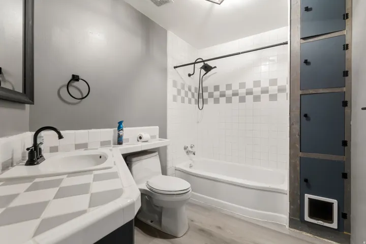 White subway tile shower surround with checkered accent band, white tub, and black shower fixtures