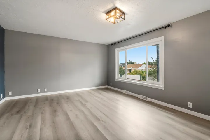 Expansive window, wood-finish flooring, contemporary ceiling light fixture, neutral wall finishes, and white trim