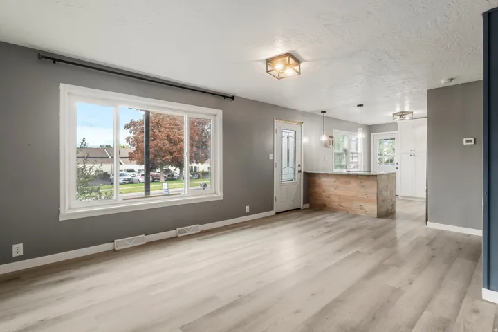 Expansive window with white trim, wood-finish flooring, two modern flush-mount light fixtures, and a peninsula with wood paneling and a light-colored countertop