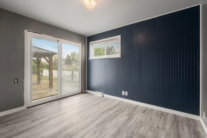 Sliding glass door, wood-finish flooring, accent wall with vertical paneling, white trim, and a window with blinds