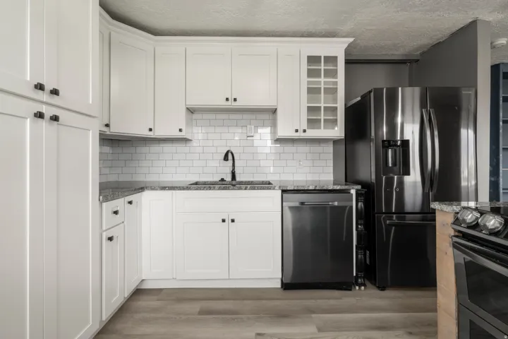 Bright kitchen featuring white shaker cabinetry, stone countertops, a subway tile backsplash, stainless steel appliances, and wood-finish flooring