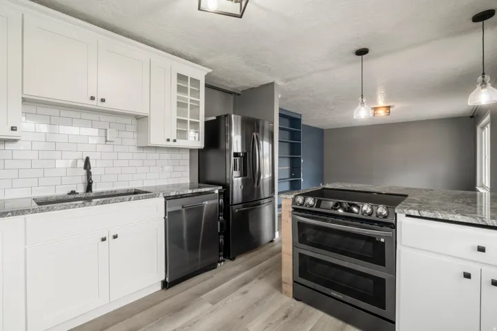 White shaker cabinetry with dark hardware, subway tile backsplash, stainless steel appliances, light-toned wood-finish flooring, and pendant lighting