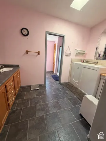 Spacious laundry room featuring slate-finish tile flooring, white front-load washer and dryer, wood-finish cabinetry with countertop workspace, and a wall-mounted towel bar