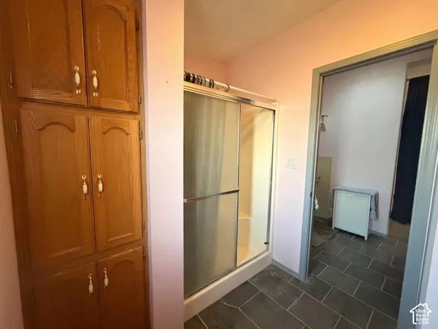 Primary Bathroom featuring a frameless sliding glass shower enclosure with brushed metal hardware, dark tile flooring, and dual vanity cabinetry with polished chrome fixtures