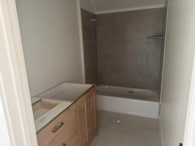 Undermount tub with subway tile surround, wood-finish vanity with drawer storage, and tile flooring