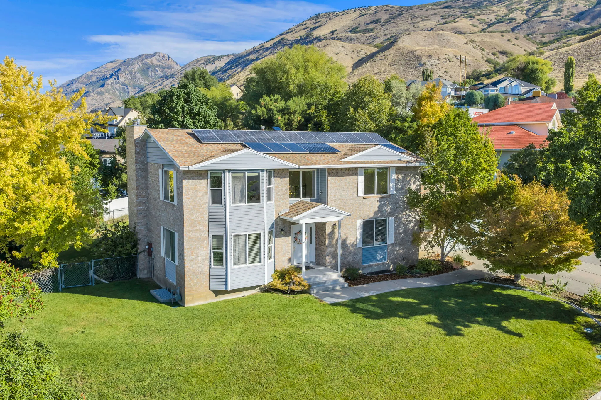 Upper East Lindon Two Story, Brick and siding exterior with solar panels, mature landscaping, and a mountain backdrop