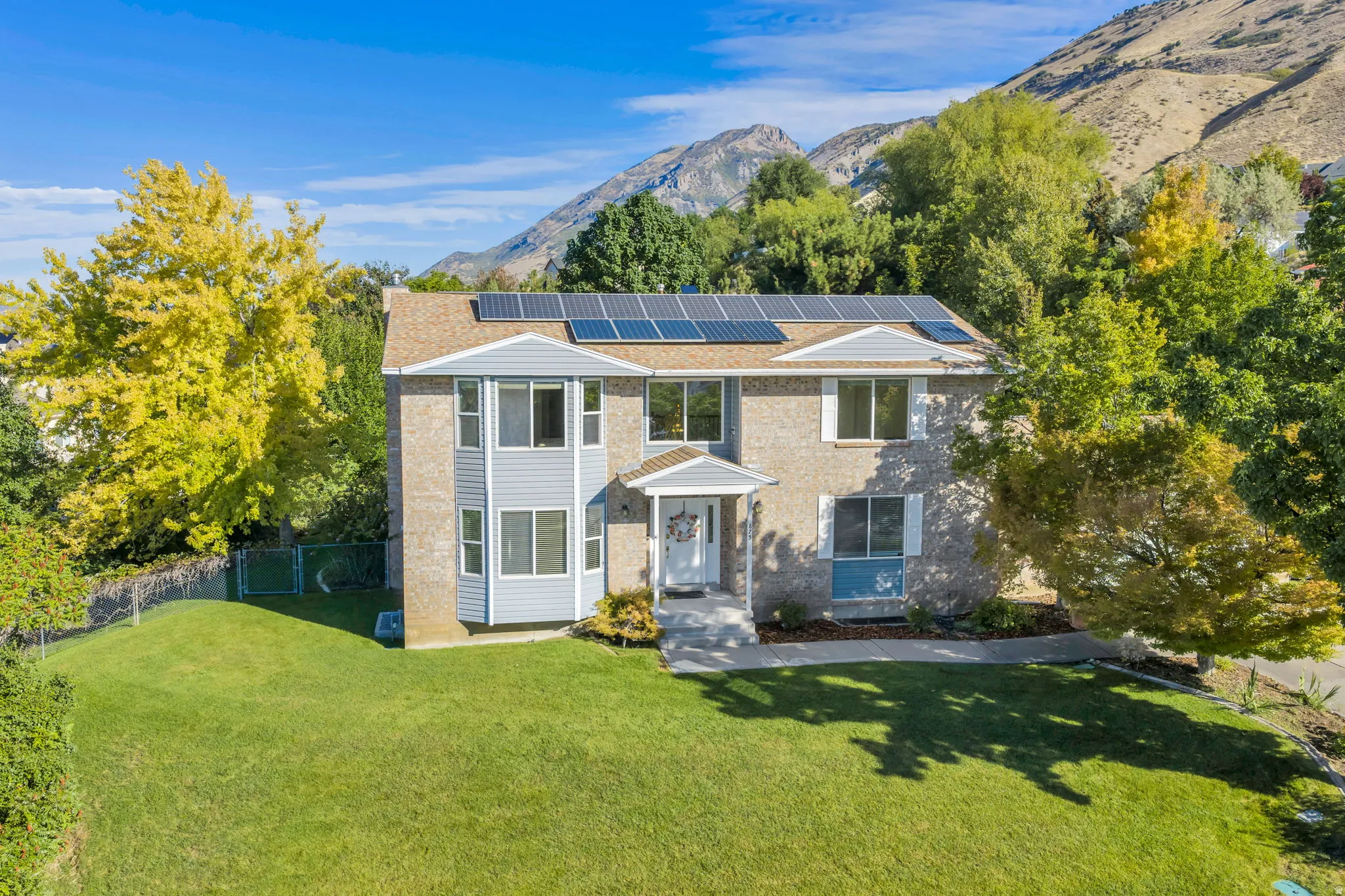 Two-story residence with a stone and siding exterior, bay window, front entry with covered porch, solar panels, and a landscaped front yard