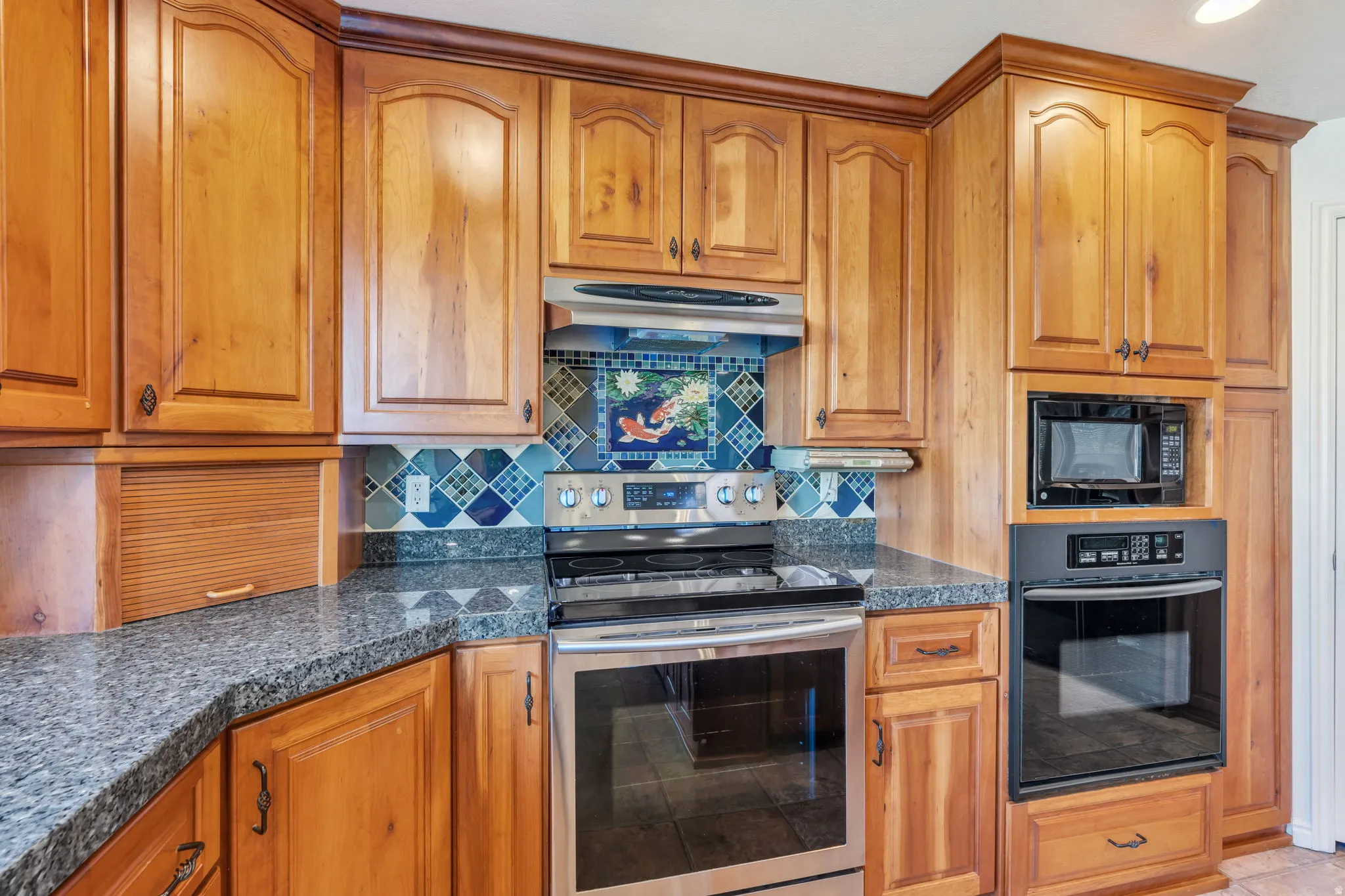 Wood cabinetry with crown molding, granite-style countertops, stainless steel range, and tile backsplash
