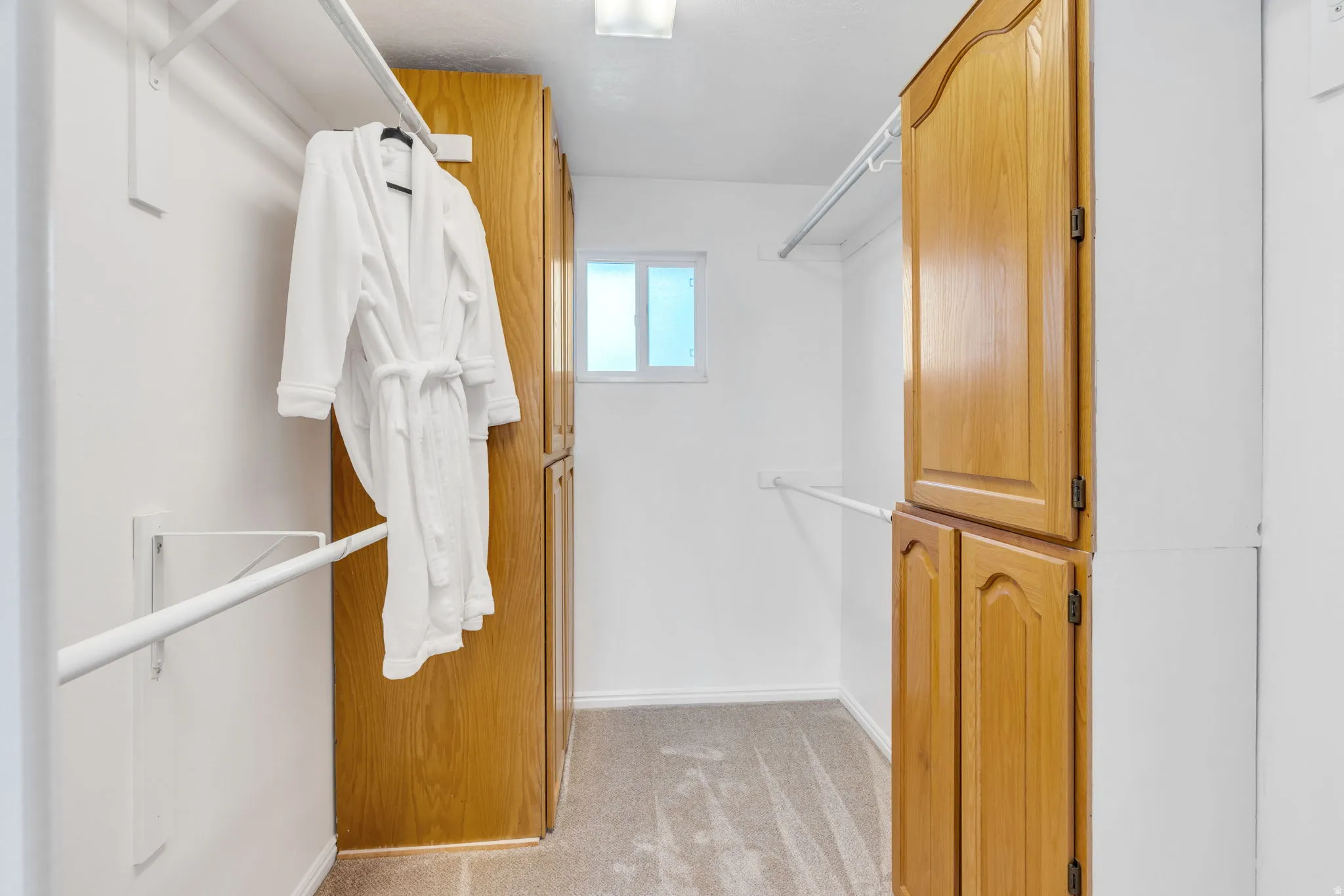 Primary Suite Closet featuring light wood-finish cabinetry, white shelving, and a small window for natural illumination