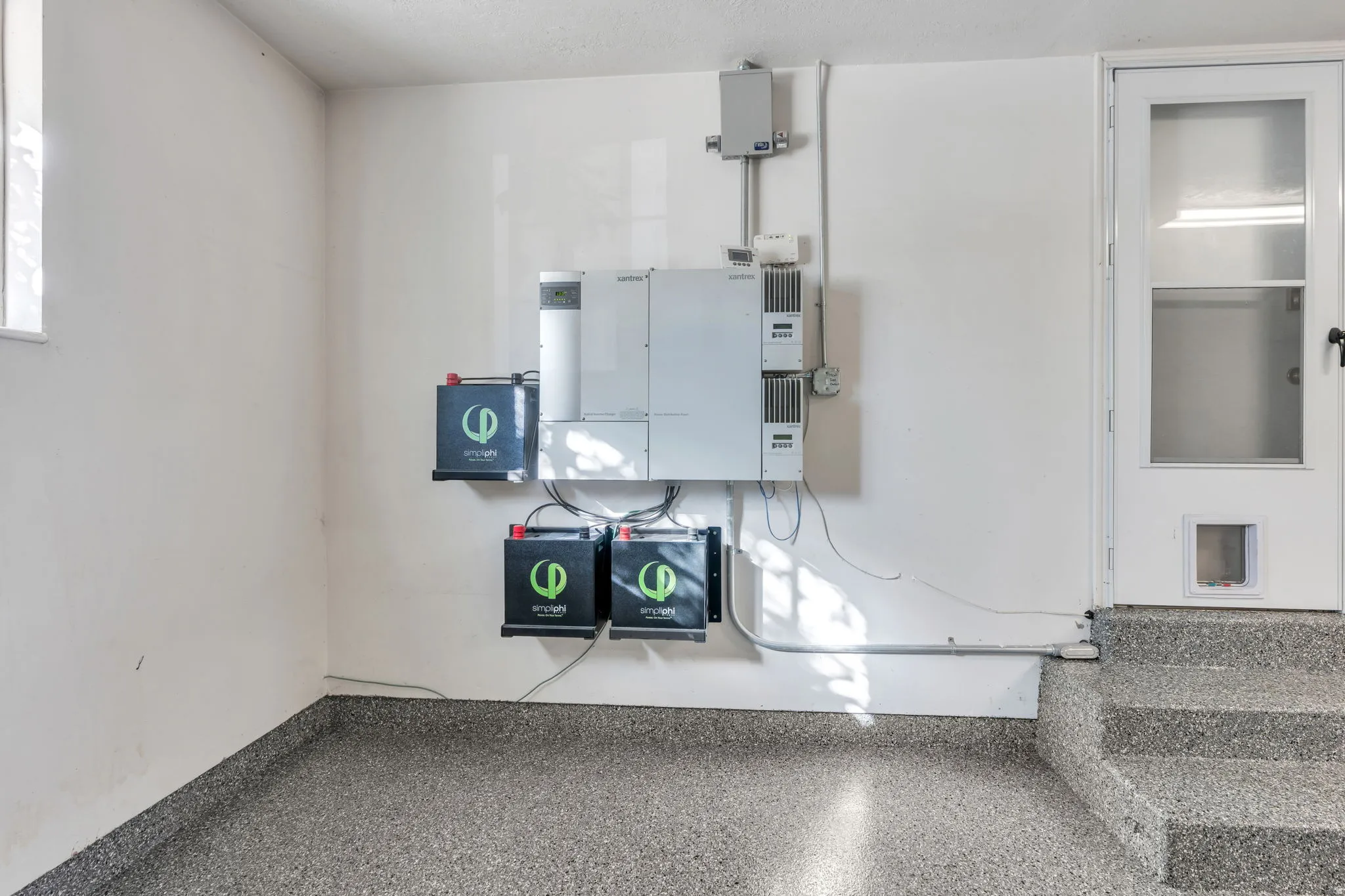 Garage with New Epoxy-coated floor, New battery storage system,/inverter system, white paneled door, and built-in steps