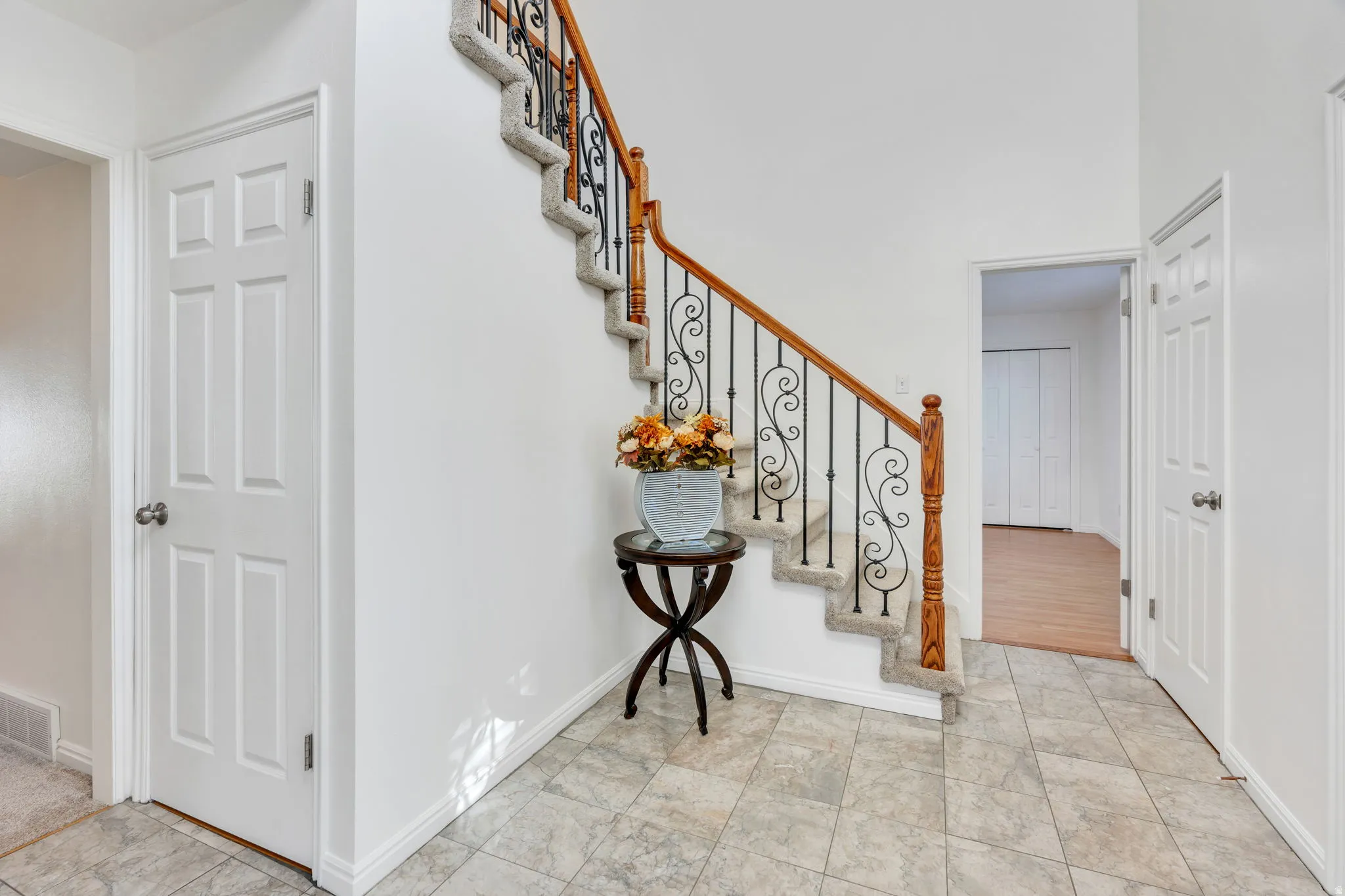 Foyer with marble tiled entryway flooring, staircase with carpeted treads, wrought iron balusters, wood handrail, and white paneled doors