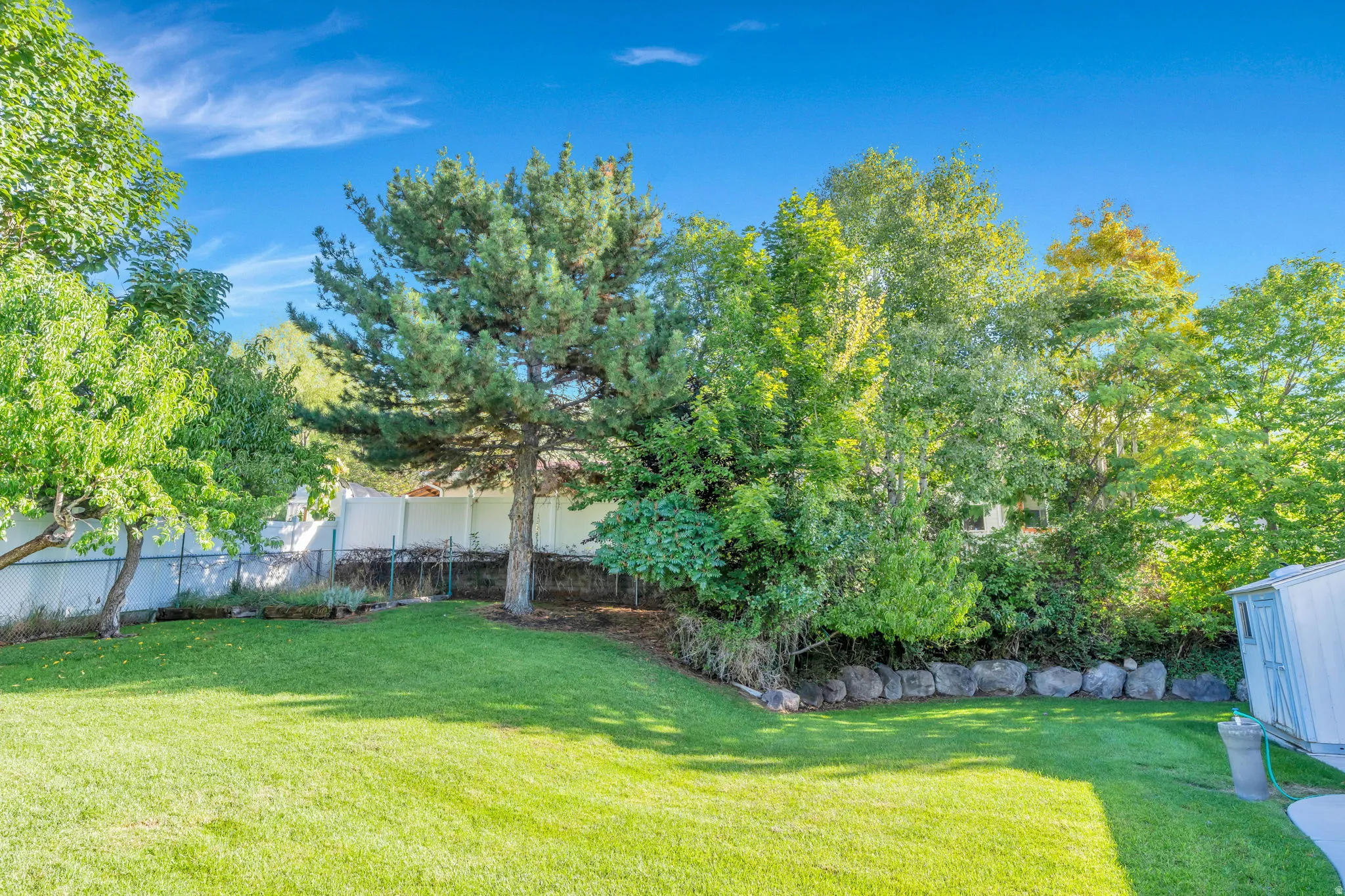Well maintained lawn area, mature trees, rock retaining wall, and privacy fencing