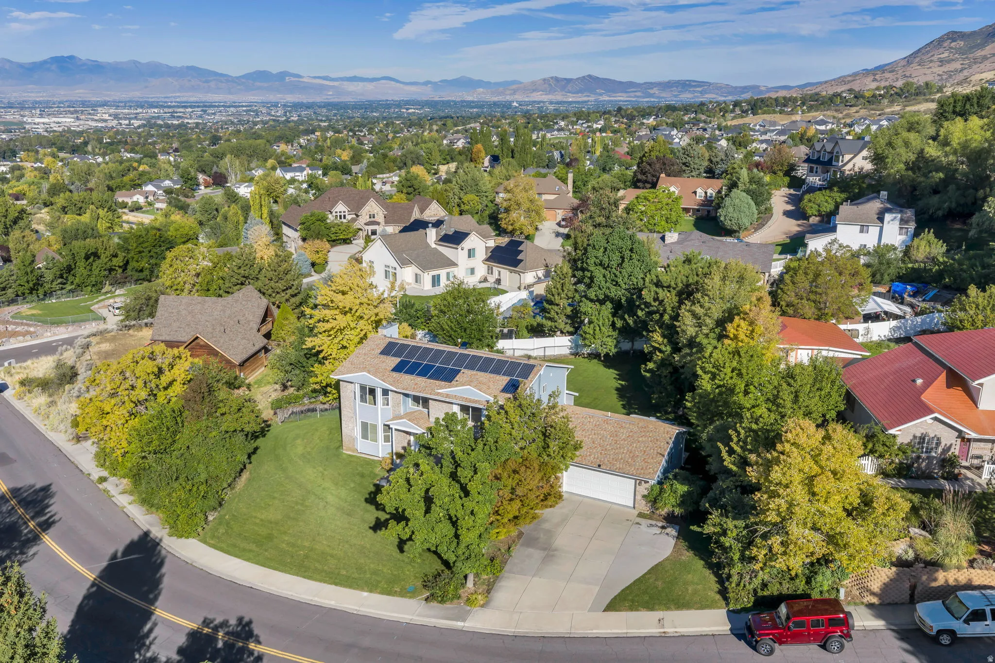 Large Residential property featuring solar panels, a two-story elevation, an attached garage, a paved driveway, and established landscaping