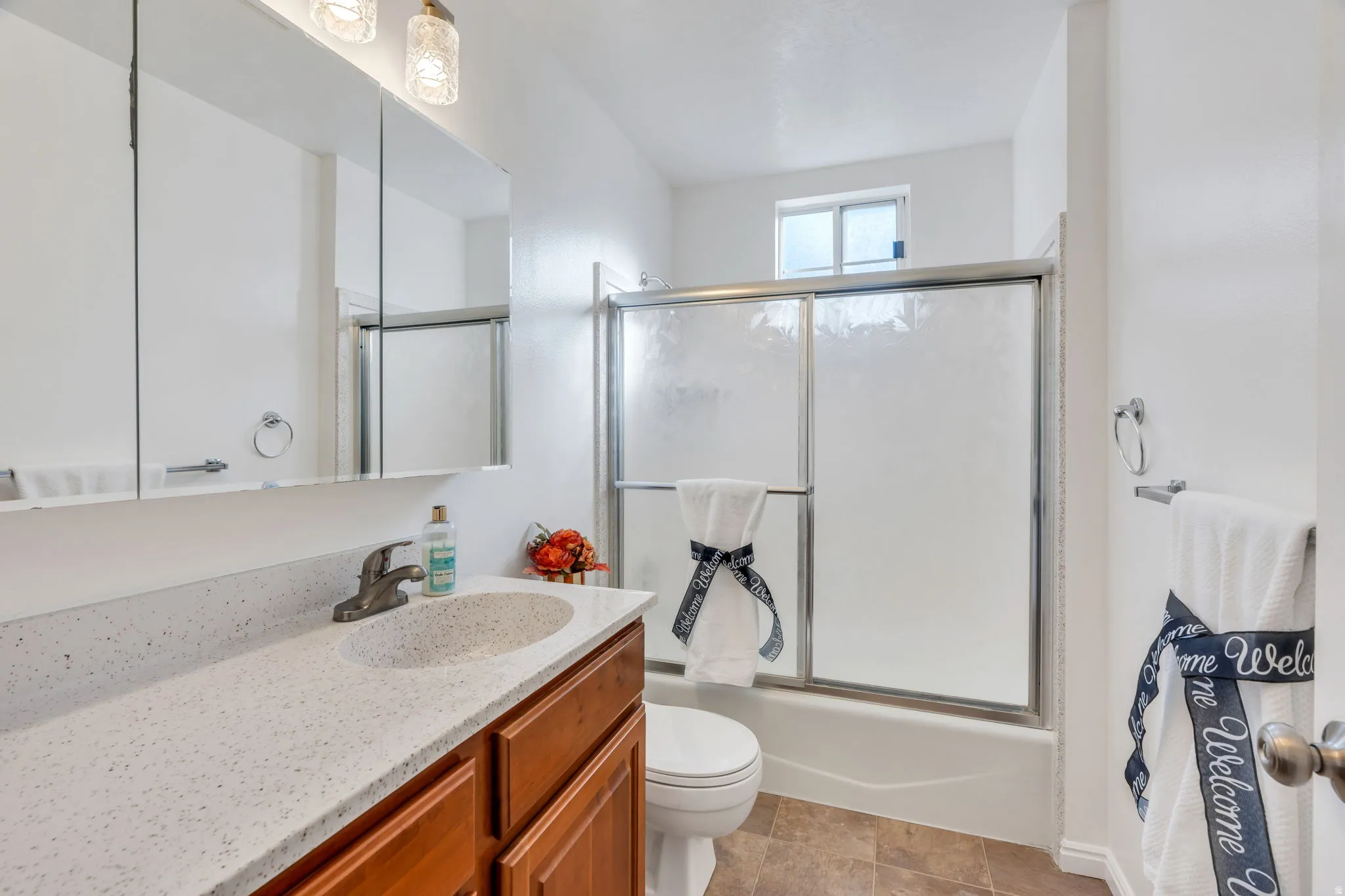 Hall bathroom with tub/shower, vanity with a speckled countertop and an integrated sink, framed by a three-panel mirrored medicine cabinet