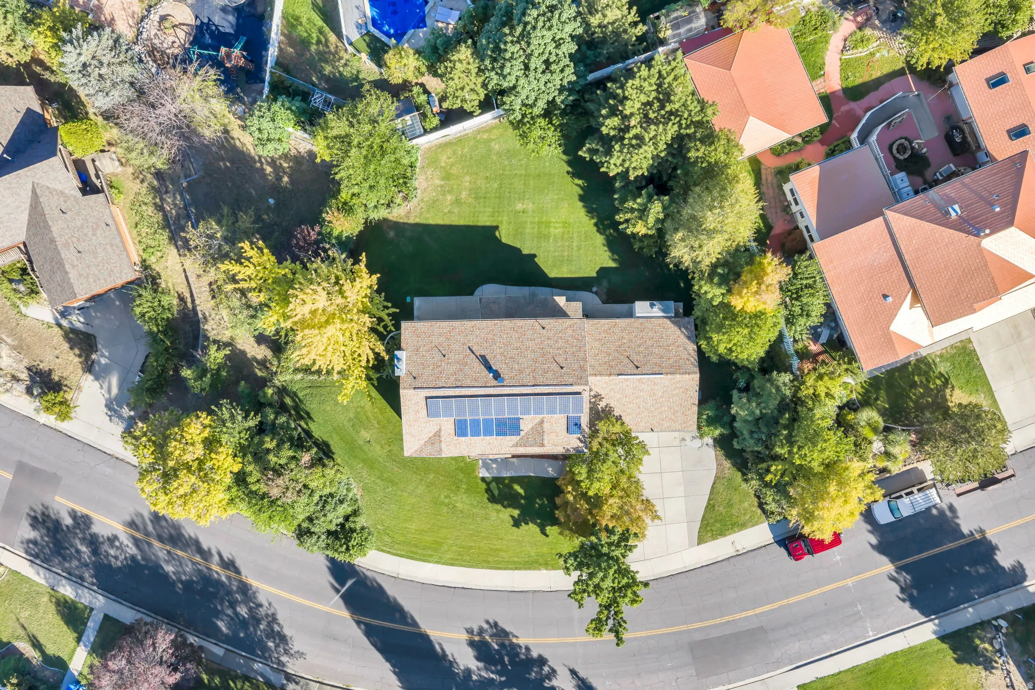Two story residence featuring a brown shingle roof, solar panel array, expansive grassy yard, and mature perimeter trees