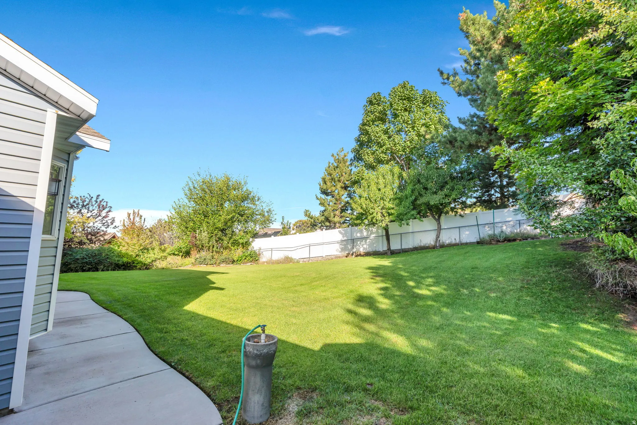 Secluded back yard with Expansive lawn area, a white privacy fence, mature trees, and a concrete pathway