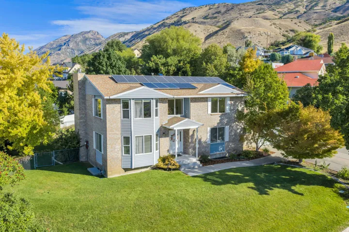 Upper East Lindon Two Story, Brick and siding exterior with solar panels, mature landscaping, and a mountain backdrop