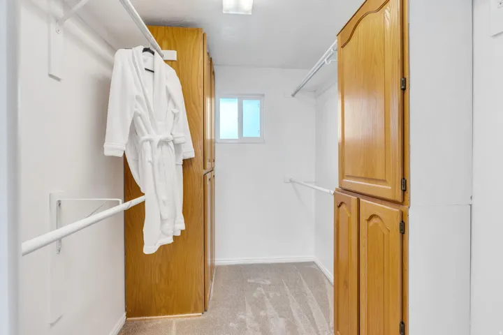 Primary Suite Closet featuring light wood-finish cabinetry, white shelving, and a small window for natural illumination